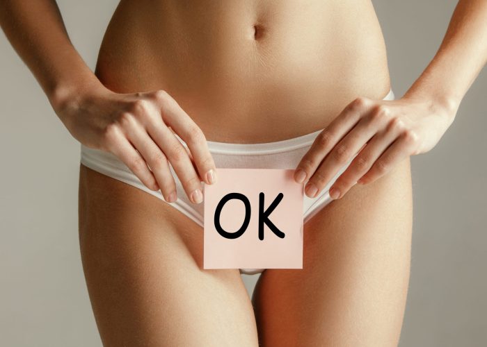 Woman health. Female model holding card near stomach. Young adult girl with paper with OK sign or symbol isolated on gray studio background. Cut out part of body. Medical problem and solution.